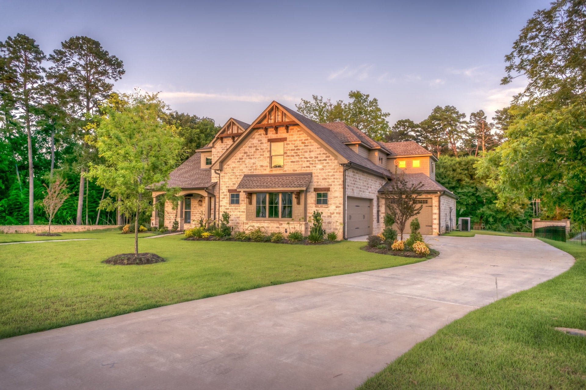 Photo of brown stone home at sunset with lush green yard.  