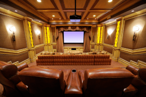 Image of luxury home theater with gold curtains and finishes and brown luxury theater seating.
