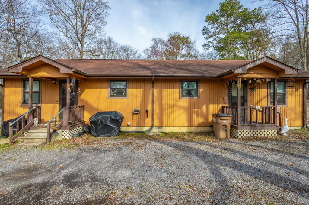 Front of 315 Old Lake Road a 2 unit duplex with mustard colored siding 1 story and brown shingled roof.