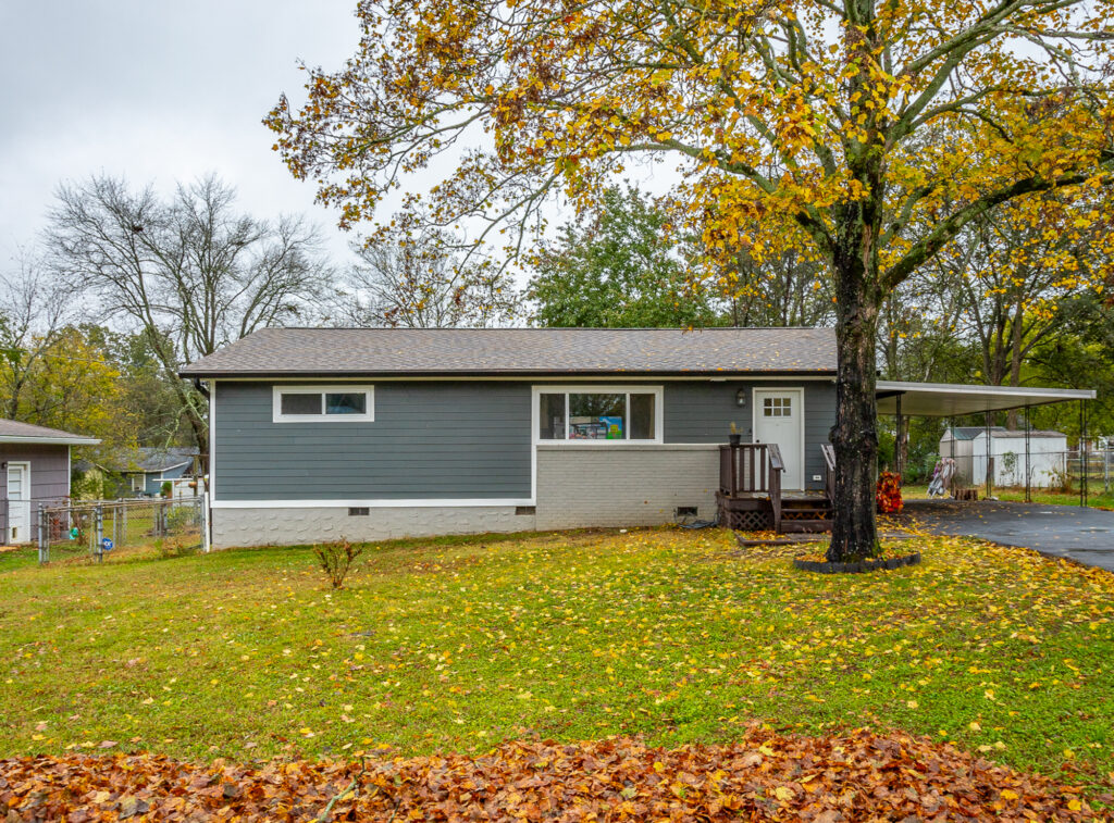 Front of 5328 Spriggs Street a simple one-story home for sale with blue siding and carport