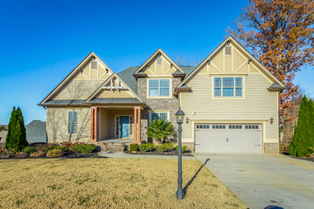 Front of 7538 Sandy Creek Lane a 4 bedroom craftsman style home for sale on level lot with stone facade and yellowish beige siding